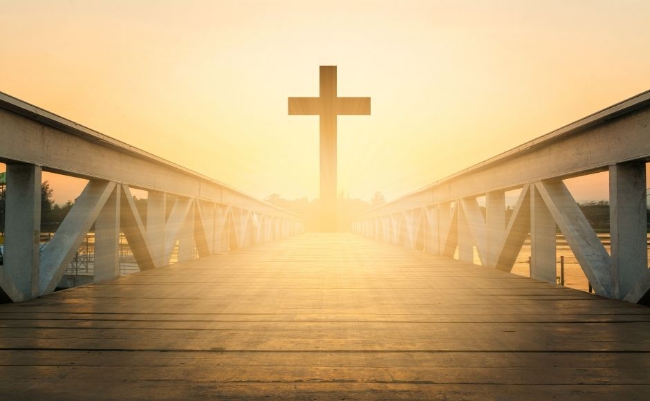 A cross standing at the end of a bridge at golden hour before sunset.