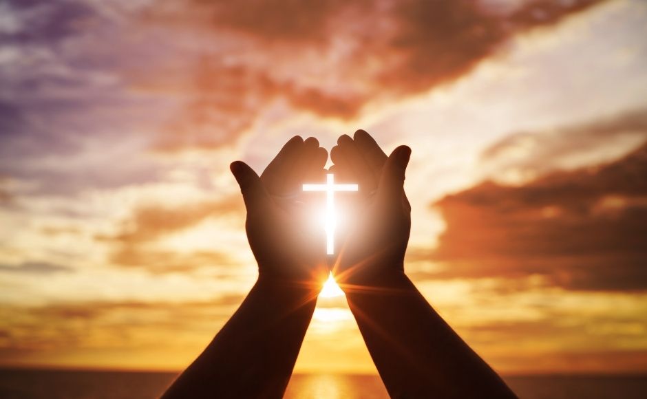 Praying hands with the shape of the cross formed by the sunshine streaming through the hands