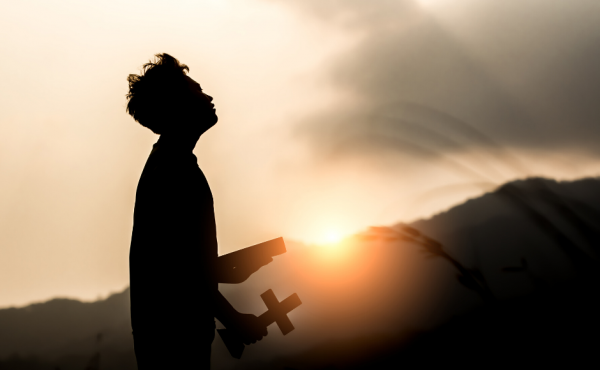 Man holding a cross outdoors at sunset