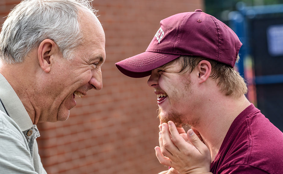 Older man smiling at younger man with Down's Syndrome, who is smiling back