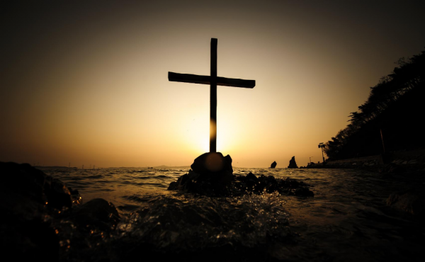 A cross sitting on a rock surrounded by crashing waves at sunset