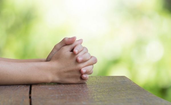 Hands praying on a table outside on a sunny day