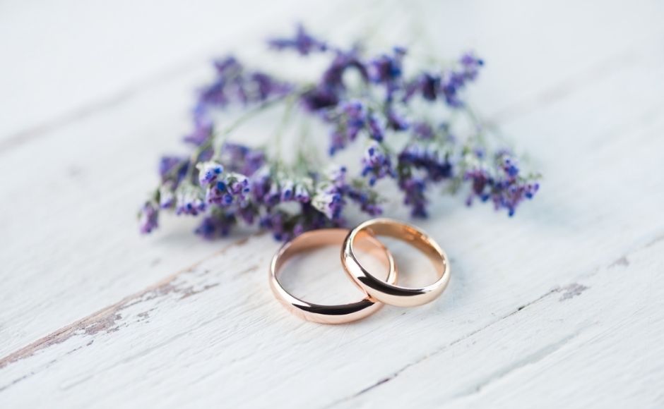 Two wedding rings on a table beside purple flowers