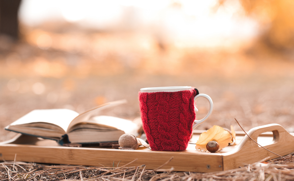 Cup of tea and a book on a tray sitting outside on the autumn leaves