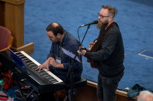 A man plays guitar and sings alongside a pianist