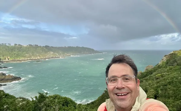 Rev Justin Taylor pauses for a photograph with a rainbow over the Guernsey coast in the background.