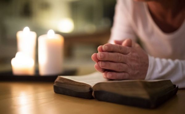 Woman's praying hands on a Bible with candles in the background