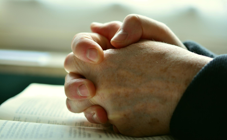 Man's hands praying on a table