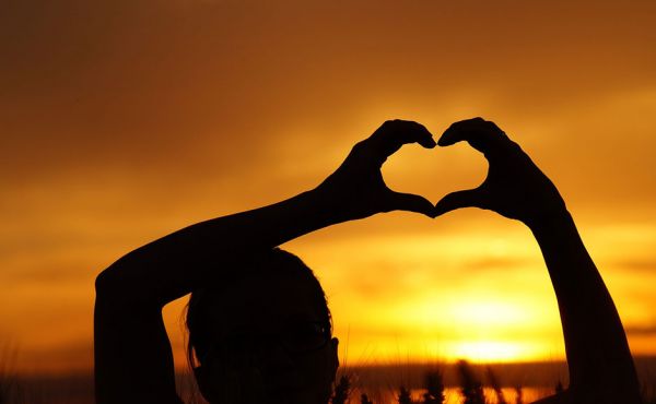 Hands forming a heart against a sunset