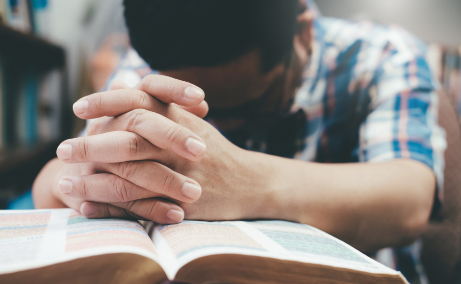 Man's hands praying over a Bible