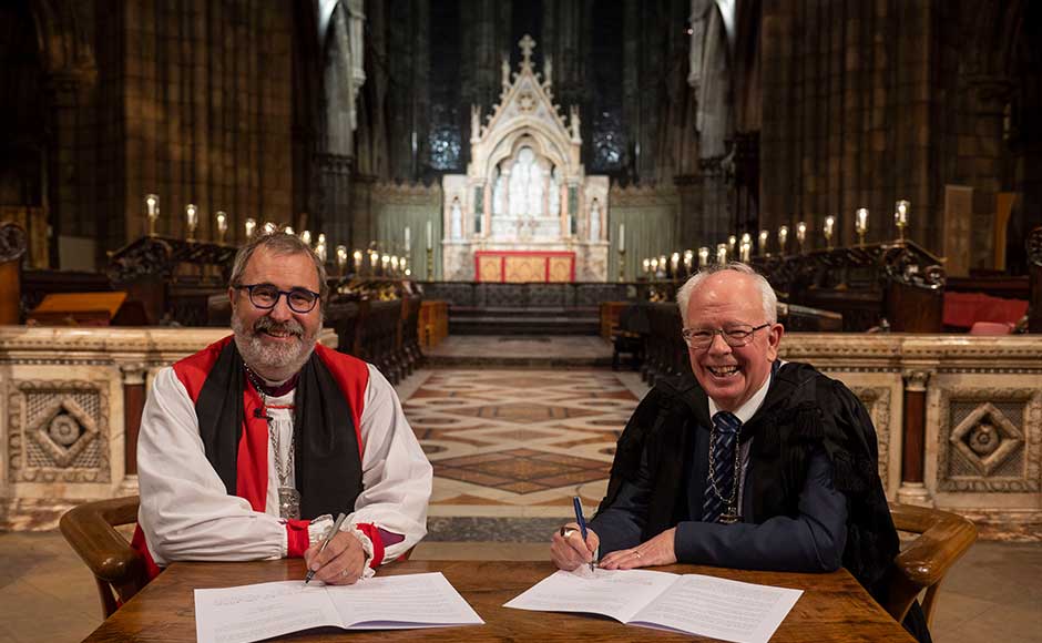 Lord Wallace and Rev Mark Strange signing a document in a cathedral
