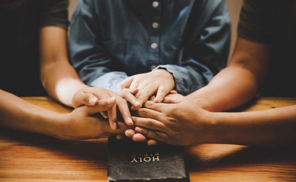 Diverse group of three people's hands hold over a Bible.