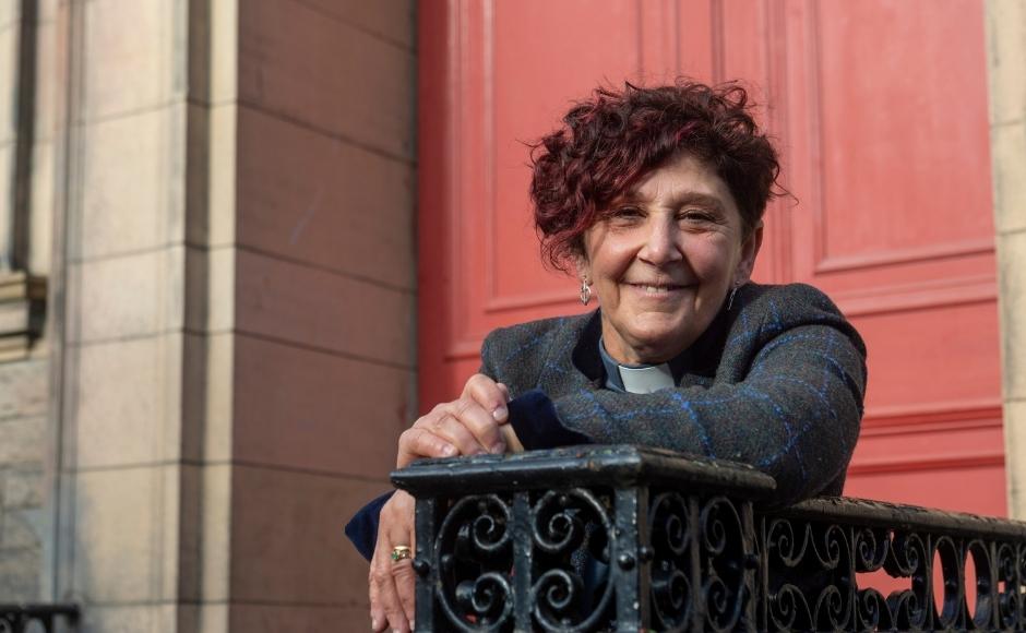 Rev Sally Foster-Fulton smiling in front of a door leaning on a bannister