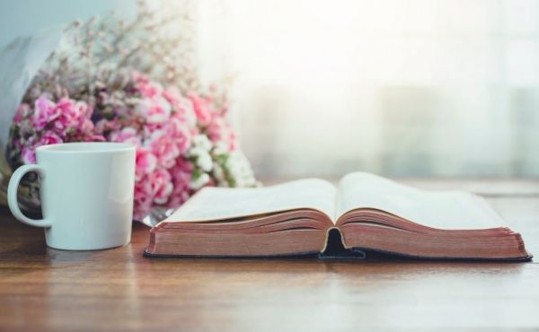 Open Bible on table with a cup of coffee next to it and some pink flowers